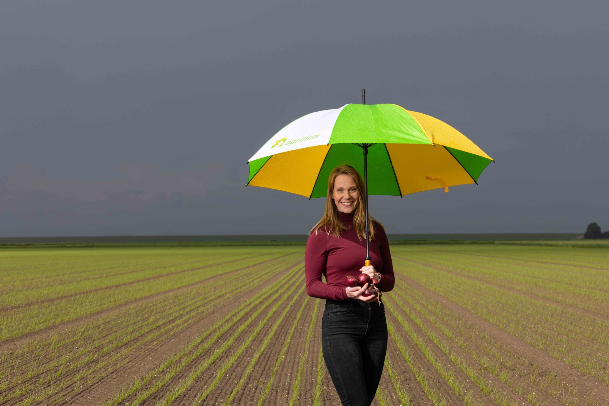 Agrifirm-medewerker met rode uien en een groen-gele paraplu op een akker.